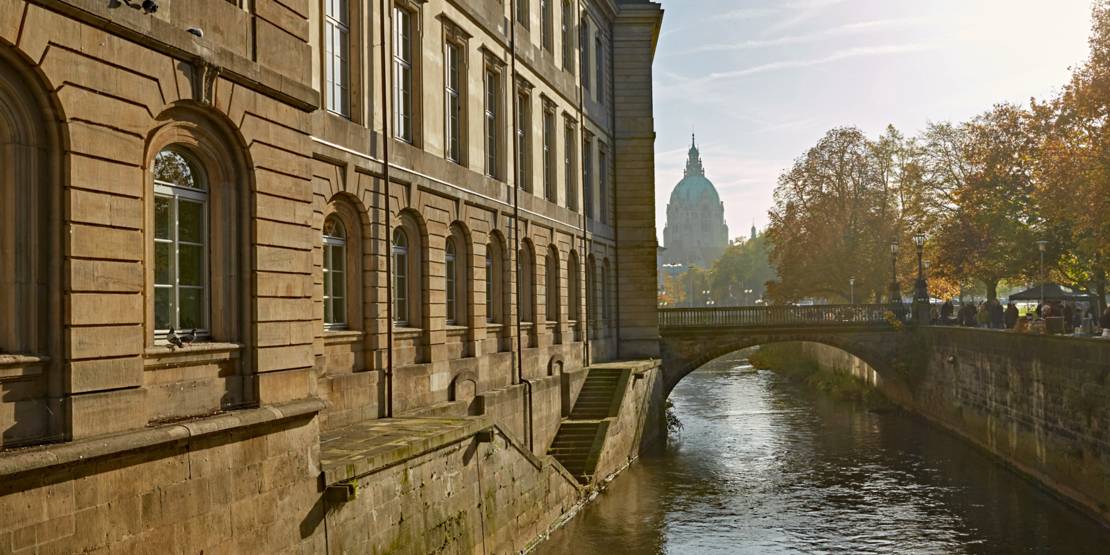 Fluss mit Uferbefestigung, links das Landtagsgebäude im Hintergrund das Rathaus.